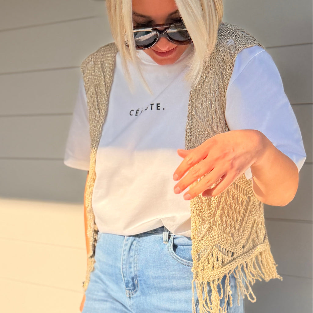 Gilet beige en maille ajourée sans manches avec franges. Léger, bohème et parfait pour un look chic et estival.