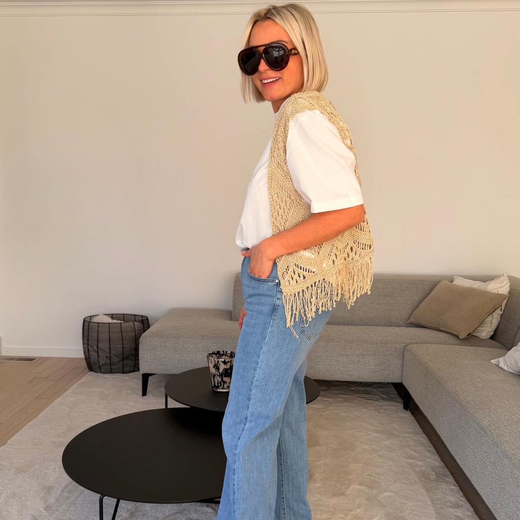 Gilet beige en maille ajourée sans manches avec franges. Léger, bohème et parfait pour un look chic et estival.