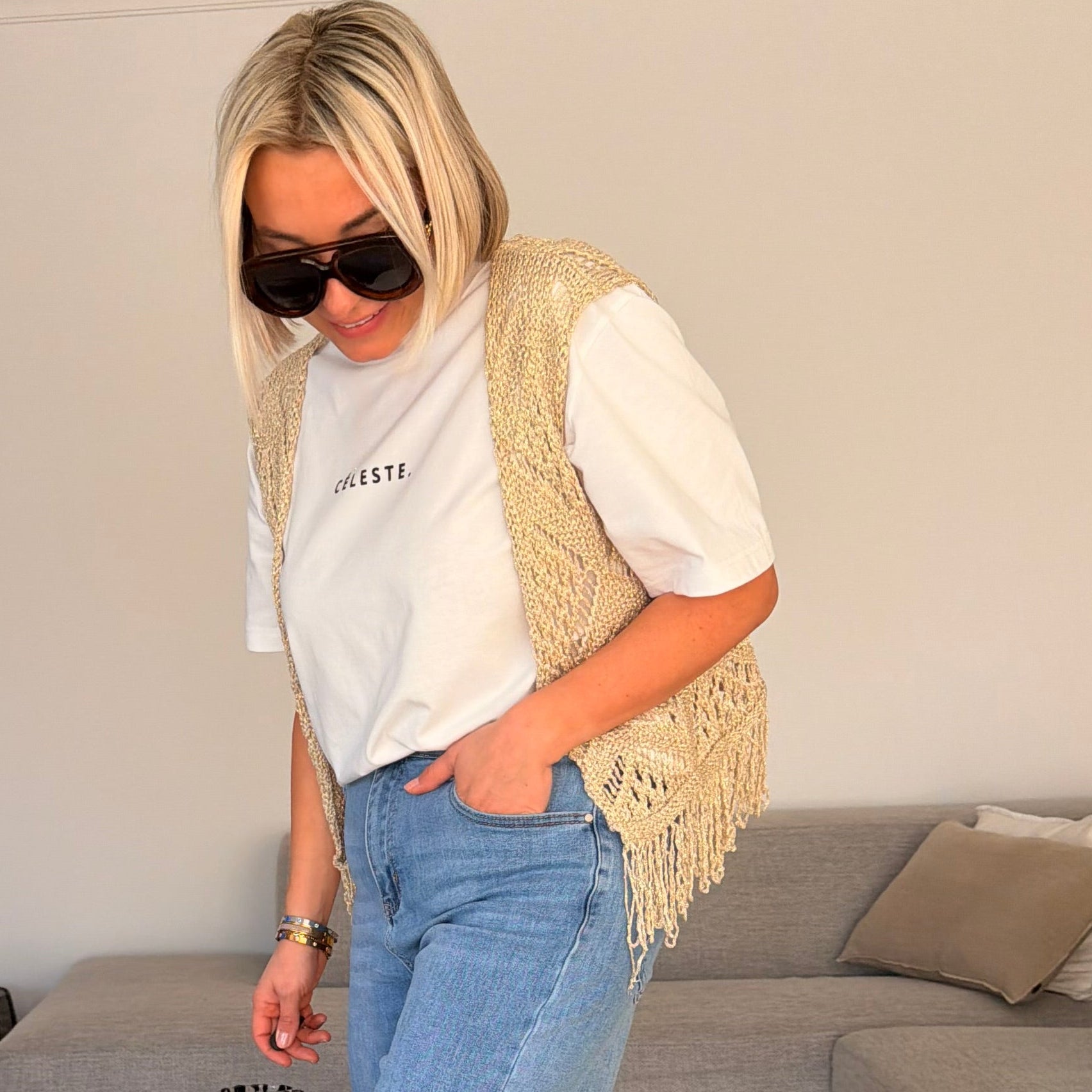 Gilet beige en maille ajourée sans manches avec franges. Léger, bohème et parfait pour un look chic et estival.