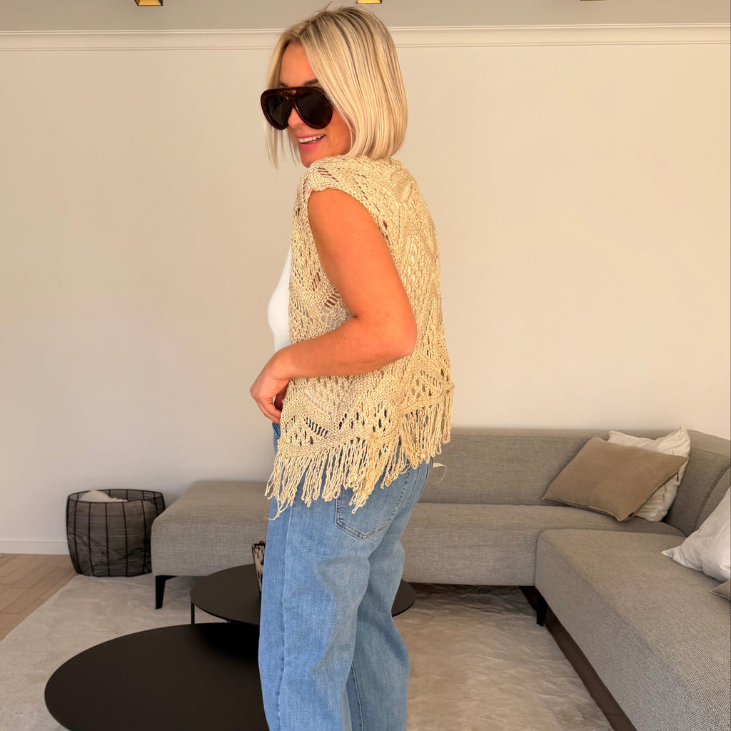 Gilet beige en maille ajourée sans manches avec franges. Léger, bohème et parfait pour un look chic et estival.