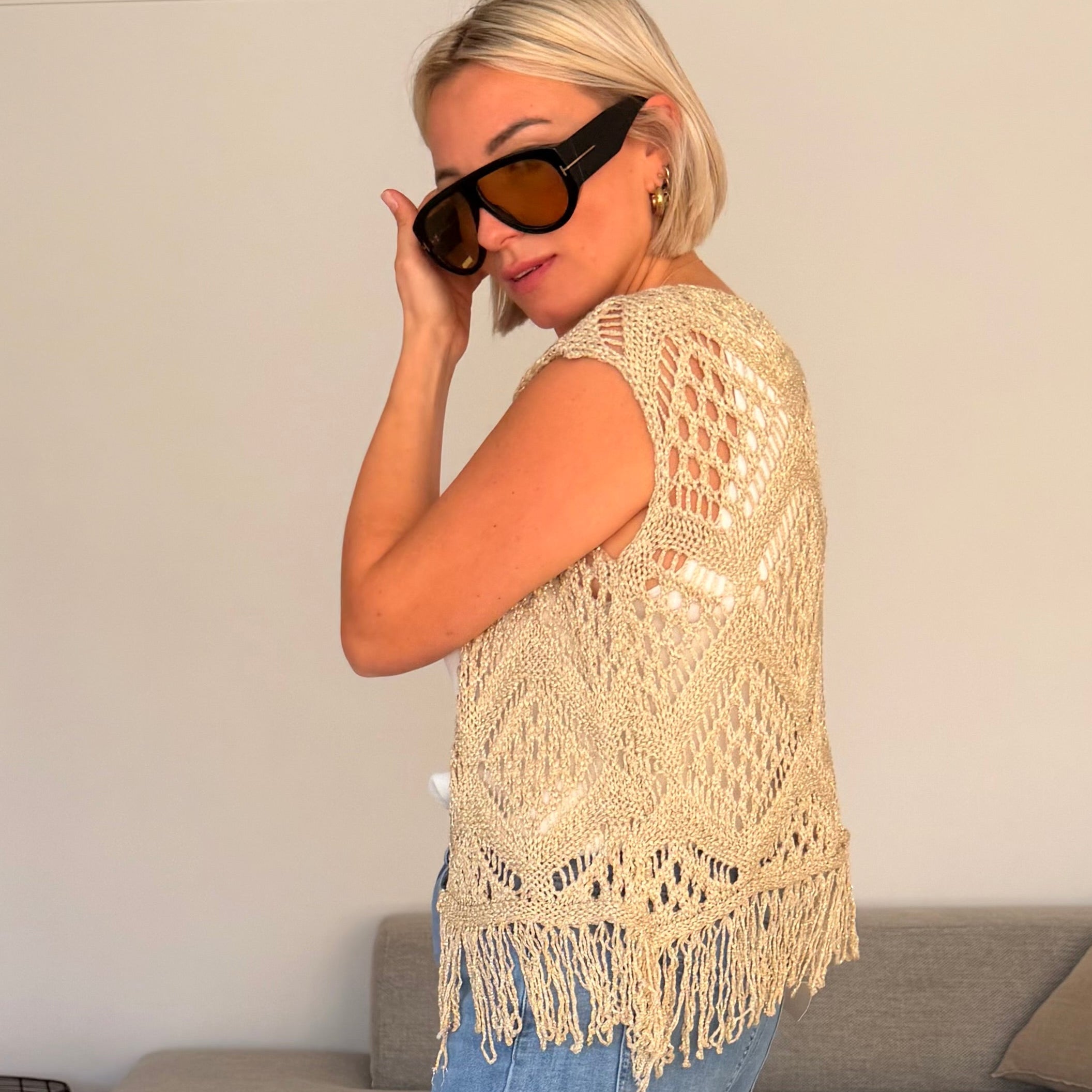 Gilet beige en maille ajourée sans manches avec franges. Léger, bohème et parfait pour un look chic et estival.