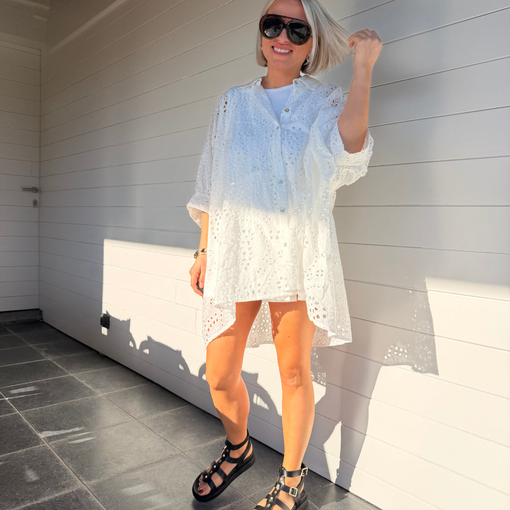Robe chemise blanche en broderie anglaise, fluide et légère. À porter en ville ou au-dessus d’un maillot pour un look estival chic.