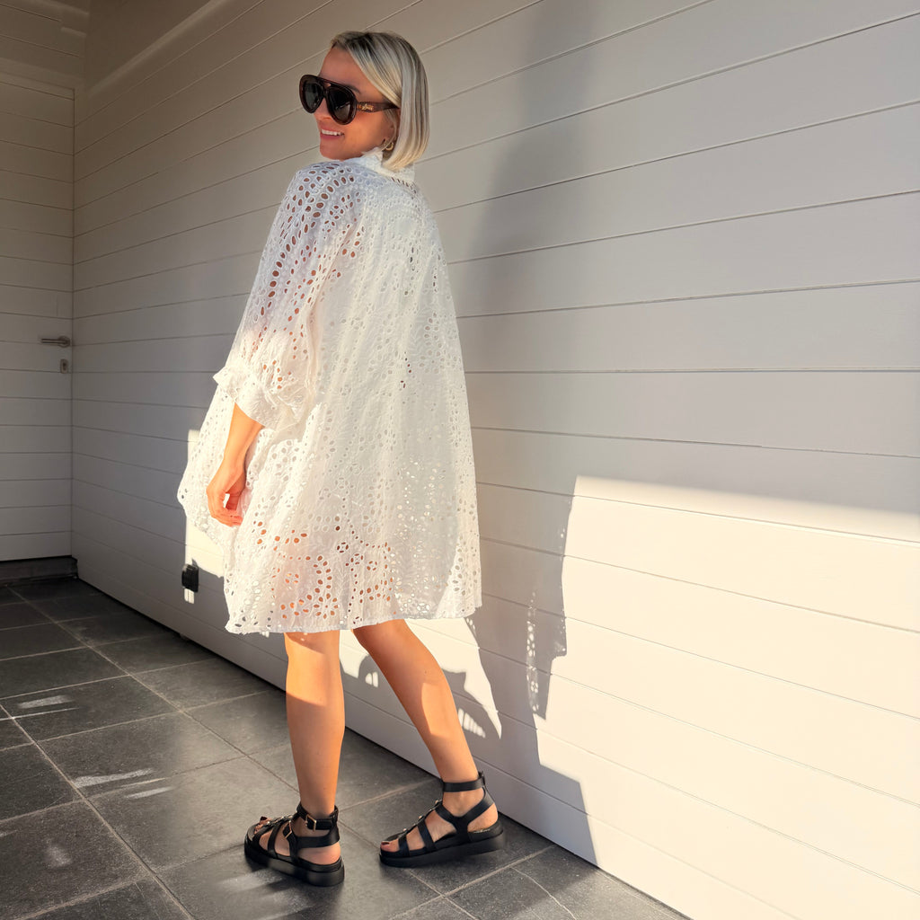 Robe chemise blanche en broderie anglaise, fluide et légère. À porter en ville ou au-dessus d’un maillot pour un look estival chic.